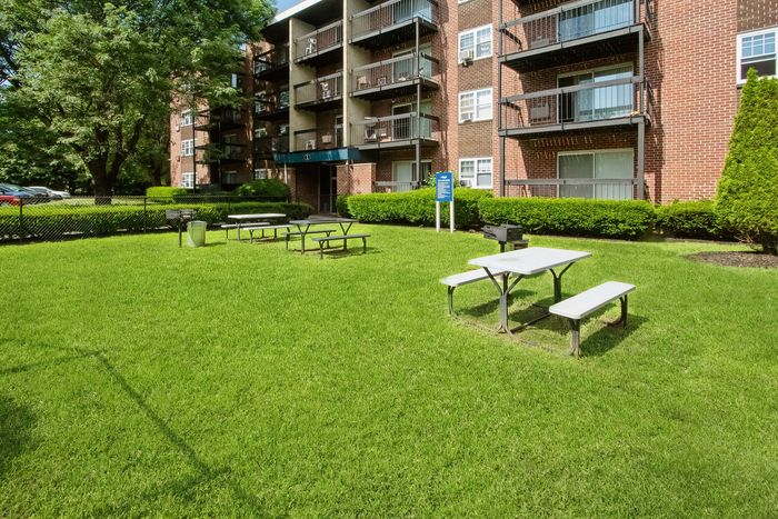 Inviting apartment complex with lush green lawn, picnic tables, and a warm community atmosphere.