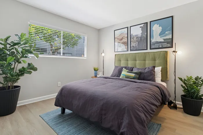 Bright and inviting bedroom with modern decor, featuring a cozy bed with a green tufted headboard, stylish wall art, and large window bringing in natural light.