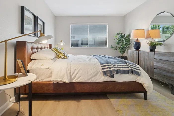 Inviting bedroom featuring a plush leather bed, modern decor, and soothing natural light through a large window.