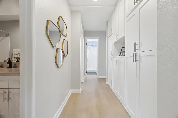 Chic hallway in modern apartment with sleek white cabinetry and stylish geometric mirrors, leading to a bright bathroom.