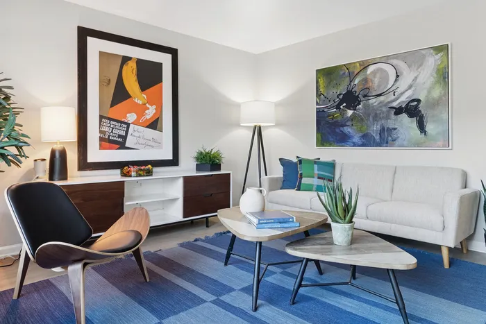Inviting and stylish living room with modern decor, featuring a cozy beige sofa, artistic wall paintings, elegant wooden chair, and vibrant potted plants on a blue rug.