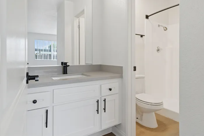Modern bathroom with sleek white cabinetry, elegant black fixtures, and a bright ambiance enhanced by natural light from a large window.