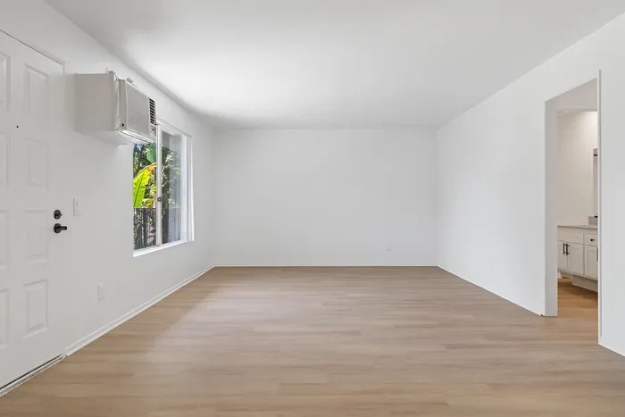 Bright and spacious living room with elegant wooden floors, large window for natural light, and modern air conditioning unit.