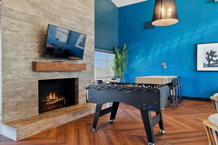 Chic lounge with modern foosball table, cozy fireplace with TV, and vibrant blue accent wall creating a warm and inviting atmosphere.