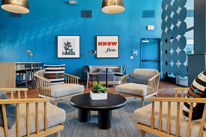 Vibrant lounge area with modern wooden chairs, colorful cushions, and a bold blue wall featuring inspiring artwork.