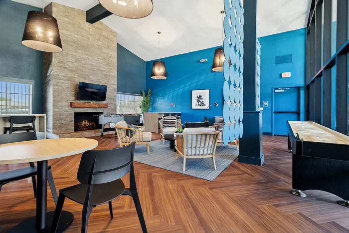 Chic communal lounge with modern decor, featuring warm wood flooring, stylish seating, and a cozy fireplace against blue accent walls.