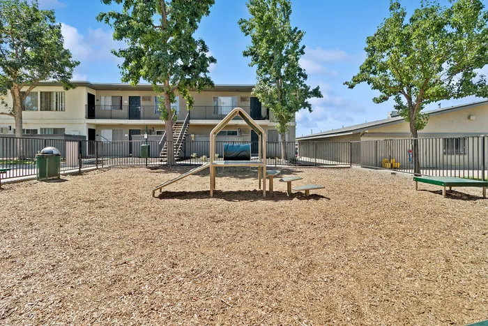 Inviting apartment complex with modern playground set amidst lush greenery and clear blue skies.
