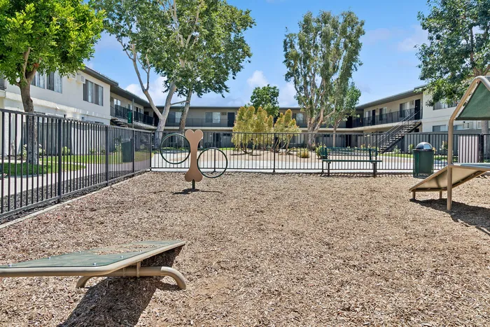 Charming pet-friendly apartment complex courtyard with a secure dog play area, surrounded by lush greenery and modern buildings.