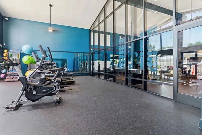 Modern gym with full-length windows, featuring cutting-edge exercise bikes, treadmills, and vibrant blue walls.