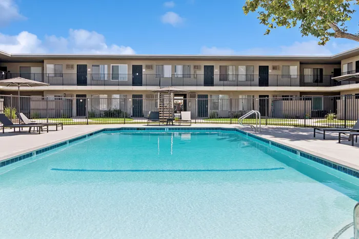 Inviting apartment complex with a pristine swimming pool, sun loungers, and modern two-story buildings, perfect for relaxation and leisure.
