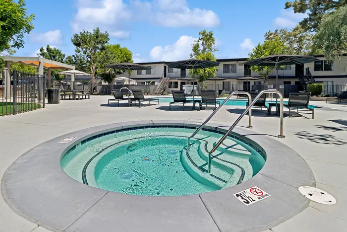 Inviting outdoor space featuring a luxurious hot tub, sun loungers, and a sparkling pool surrounded by lush trees.