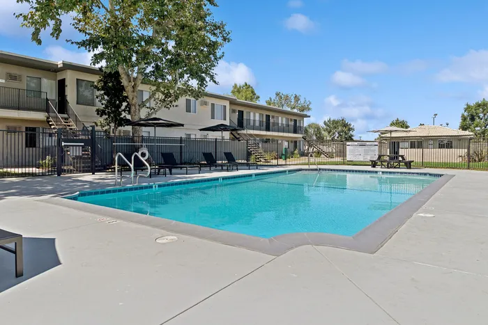 Refreshing outdoor pool area with comfortable lounge chairs and umbrella-shaded relaxation spaces against a clear blue sky background.