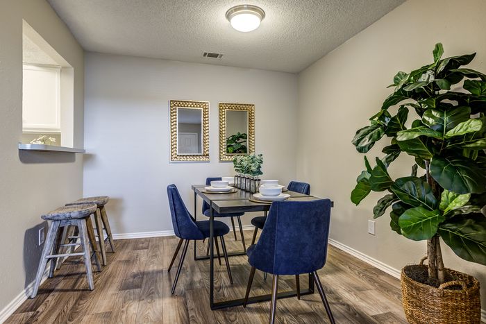 Chic dining nook with elegant blue chairs, a contemporary table, lush greenery, and stylish wall mirrors.