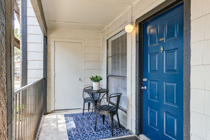 Inviting apartment entryway with a stylish blue door, cozy seating area, and decorative plant, exuding charm and warmth.