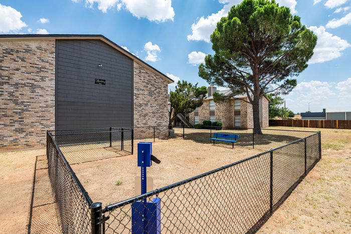 Charming brick apartment building with fenced yard, vibrant greenery, and a serene atmosphere under a sunny sky.