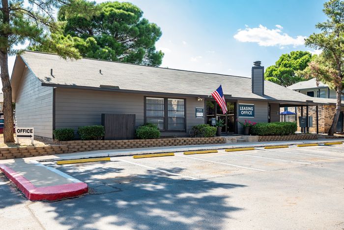 Inviting leasing office with modern siding, vibrant landscaping, and an American flag gracing the entrance.