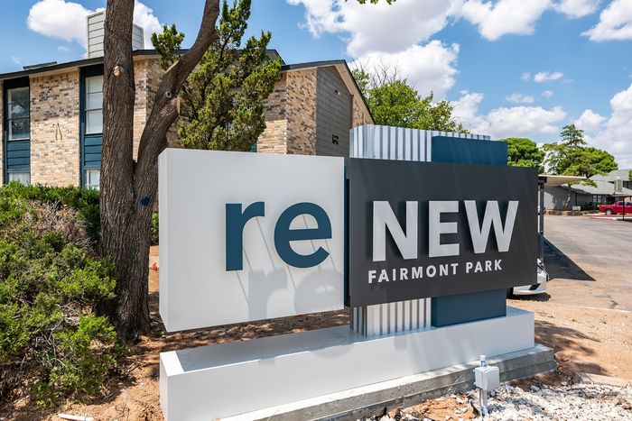 Modern apartment complex entrance with stylish 'ReNew Fairmont Park' signage surrounded by lush greenery and a bright, welcoming exterior.