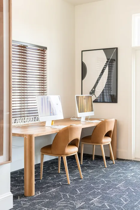 Modern home office at ReNew Howard Crossing with sleek wooden desk and stylish chairs, featuring dual computers and artistic wall decor.