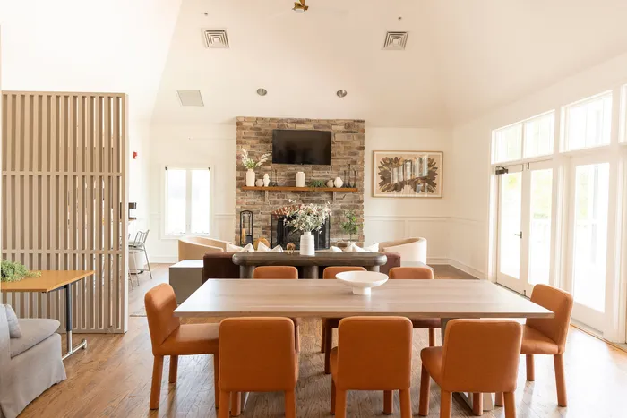 Spacious, sunlit living area at ReNew Howard Crossing with elegant stone fireplace, stylish orange chairs, and modern decor ideal for comfortable gatherings.
