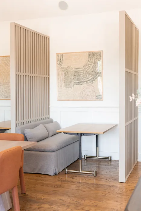 Elegant seating area at ReNew Howard Crossing with modern partition design, featuring a cozy gray sofa and stylish wooden tables, complemented by abstract wall art.