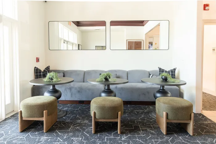 Elegant lounge area at ReNew Howard Crossing featuring a plush gray sofa with modern round tables, green ottomans, and stylish decor, creating a welcoming atmosphere.