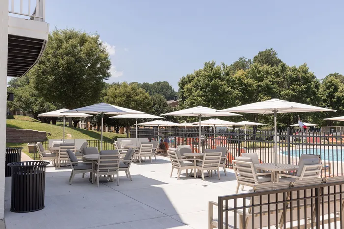 Inviting outdoor patio at ReNew Howard Crossing with stylish seating and umbrellas overlooking a sparkling pool, surrounded by lush greenery.
