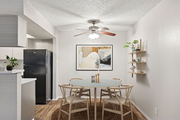 Contemporary dining area at ReNew Heights featuring a round glass table, elegant chairs, and a stylish ceiling fan, complemented by modern artwork and lush greenery.