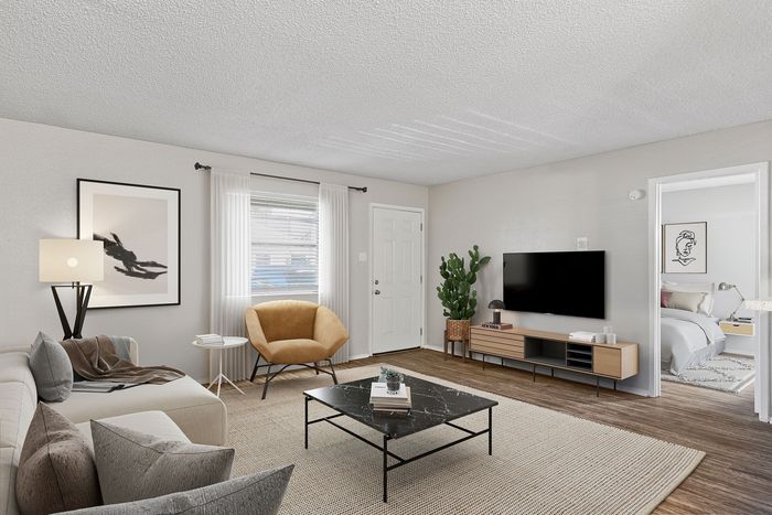 Modern living room at ReNew Heights with stylish decor, featuring a cozy sofa, sleek black coffee table, and a large TV. Natural light floods through the window, enhancing the vibrant space, complete with a chic chair and minimalist artwork.