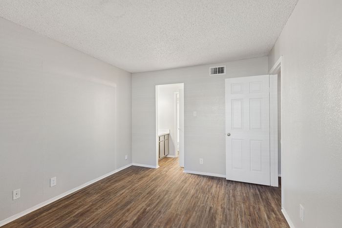 Sleek empty room at ReNew Heights with elegant wood flooring, freshly painted walls, and a view into a bright bathroom area.