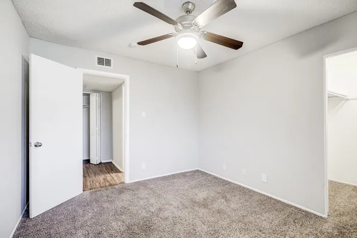 Bright and airy bedroom at ReNew Heights with soft carpet, a sleek ceiling fan, and ample closet space, perfect for modern living.