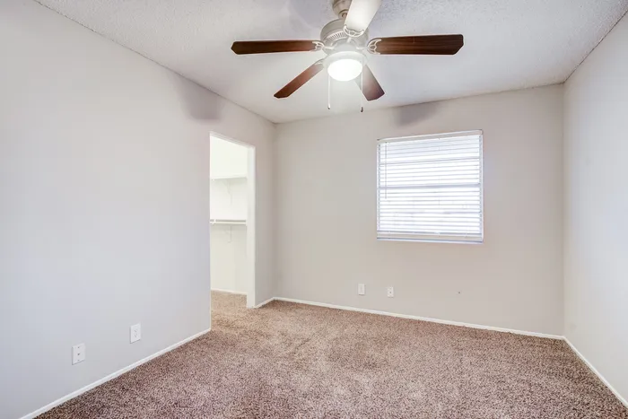 Bright bedroom at ReNew Heights with cozy carpet, ceiling fan, and a walk-in closet, offering comfort and style.
