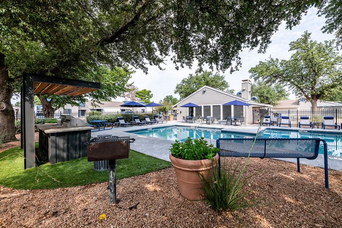 Charming outdoor pool area with lush greenery, cozy seating, and a barbecue setup, perfect for relaxation and gatherings.