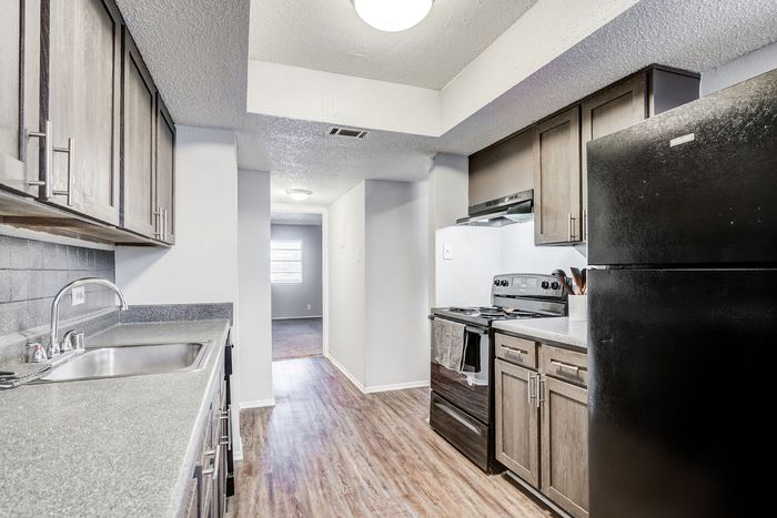 Modern kitchen at ReNew Heights with sleek black appliances, stylish cabinetry, and polished countertops leading to a bright, inviting hallway.