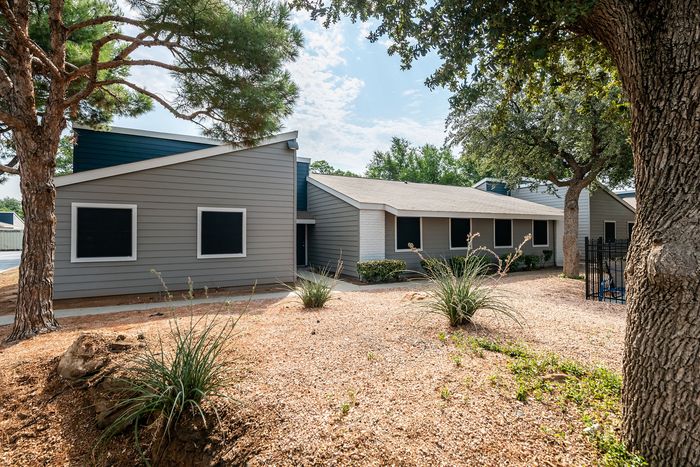 Charming modern home exterior with sleek gray siding, nestled in a beautifully landscaped yard with mature trees and desert-style plants.