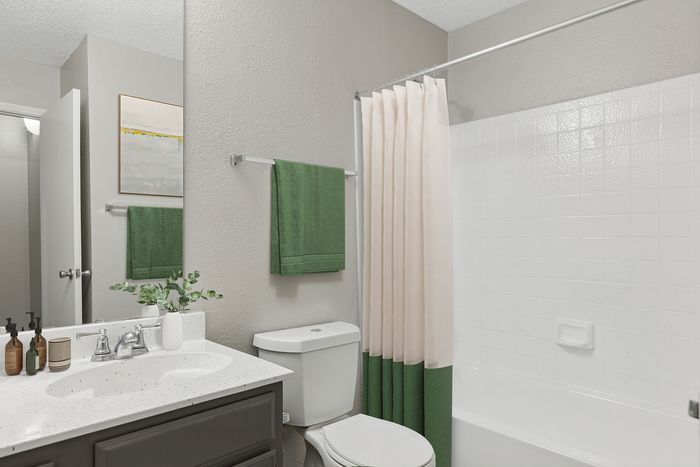 Elegant bathroom showcasing modern fixtures, a sleek vanity with a vase of greenery, and a shower with a stylish green-trimmed curtain.