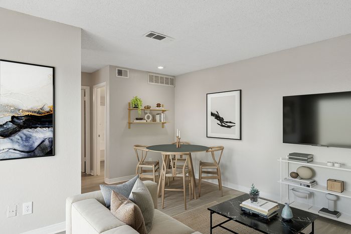 Chic, modern living room featuring a cozy beige sofa, elegant black coffee table, and stylish dining area with artistic decor.