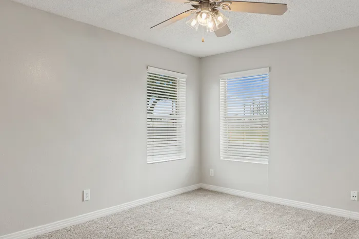 Bright and inviting corner room with large windows and plush carpet, ideal for creating a cozy retreat.
