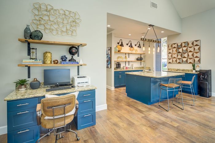 Chic open-concept home office and kitchen with stylish blue cabinetry, modern decor, and inviting wooden flooring.