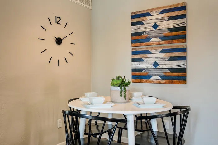 Chic dining nook with modern circular table, stylish black chairs, decorative wall clock, and vibrant art piece, perfect for cozy gatherings.