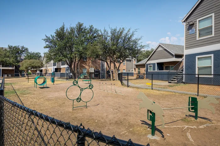 Charming apartment complex with inviting fenced dog park, featuring agility equipment and lush greenery for pet-friendly living.