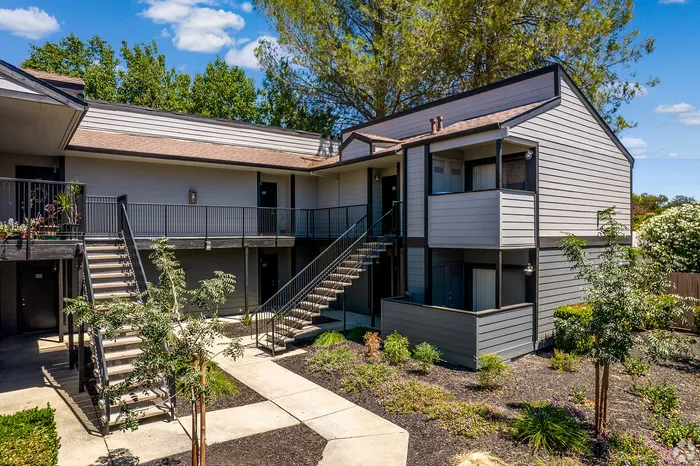 Modern apartment complex with stylish architecture, featuring lush landscaping and a well-maintained walkway under a sunny sky.