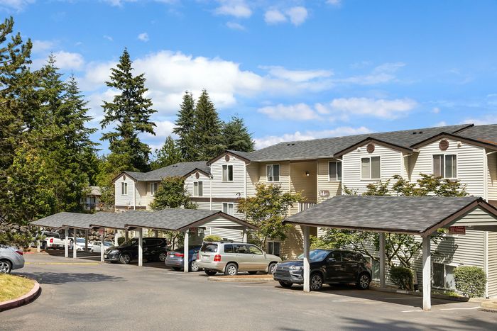 Charming apartment complex surrounded by lush greenery, featuring covered parking and modern architecture.