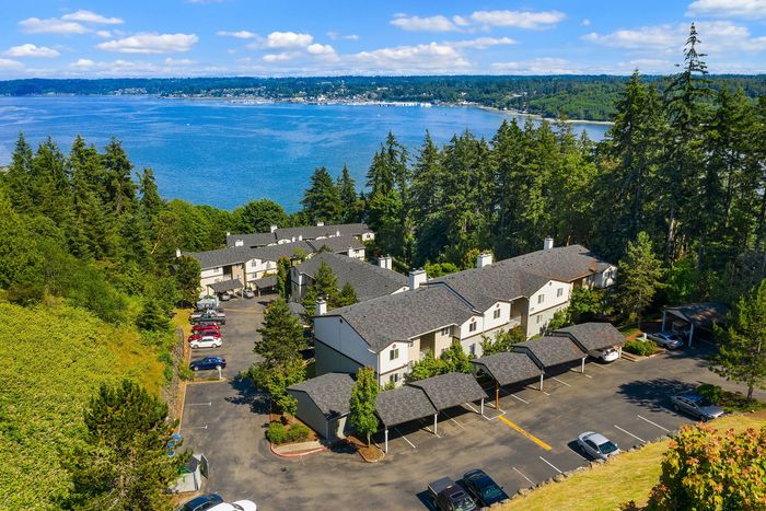 Stunning aerial view of an apartment complex nestled by lush forests with breathtaking water views, offering a tranquil living experience.