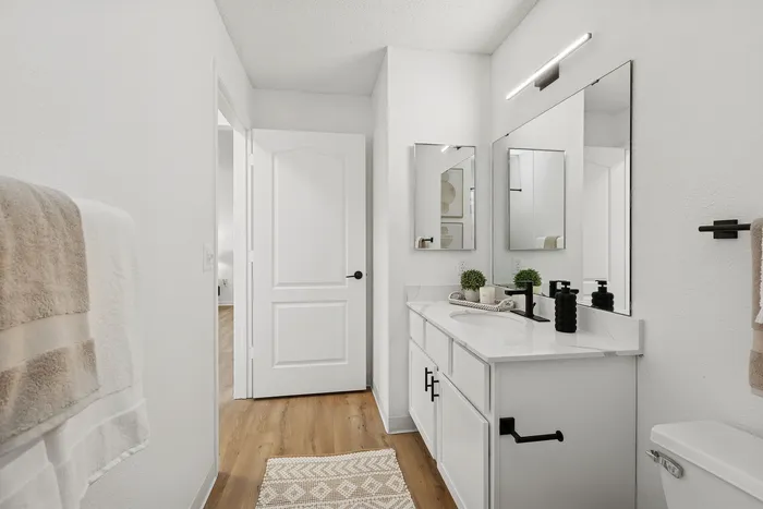 Modern bathroom with sleek white fixtures, a large mirror, and elegant decor, offering a luxurious and inviting atmosphere.