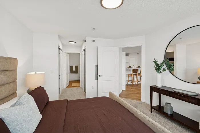 Inviting bedroom with plush bedding, elegant decor, and open doorway leading to a chic, modern kitchen with bar seating.