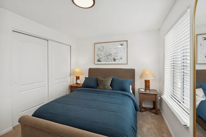 Cozy bedroom with modern decor, featuring a plush bed with blue bedding, wooden side tables, and elegant lamps.