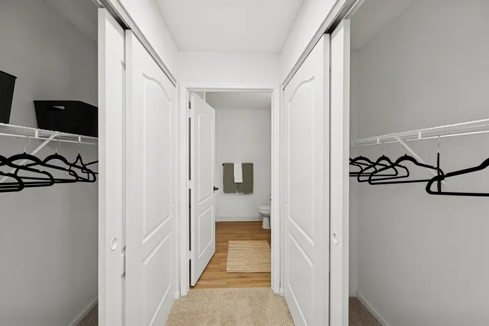 Elegant walk-through closet with sliding doors, ample storage, and a cozy carpet leading to a modern bathroom.