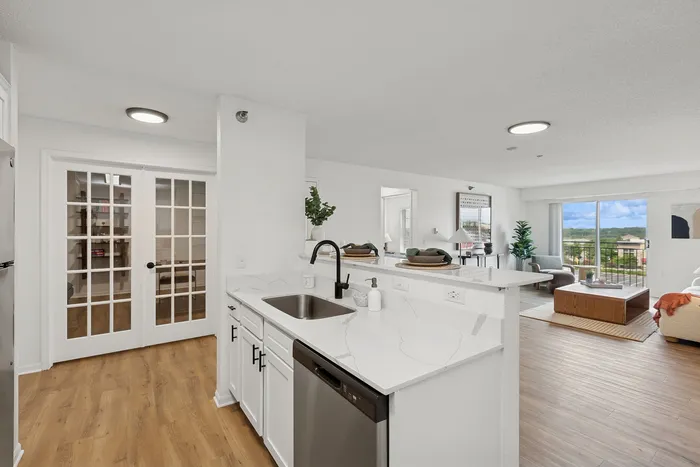Bright and modern open-concept kitchen and living area with sleek white cabinetry, stainless steel appliances, and large windows offering scenic views.