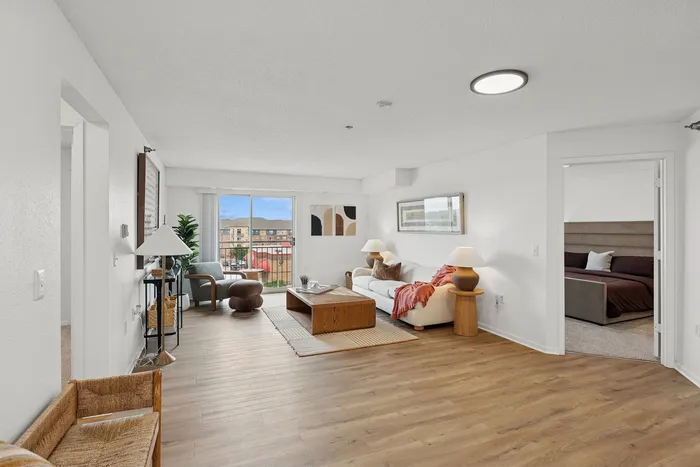 Inviting modern living room with stylish decor, plush seating, and balcony view; cozy bedroom visible through open door.