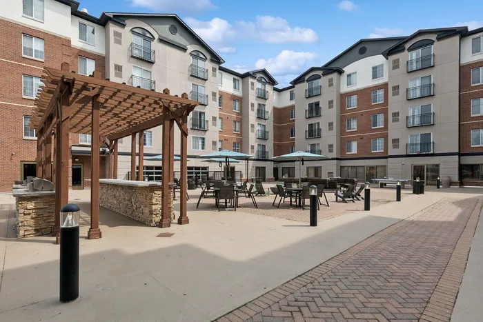 Elegant apartment complex featuring a spacious outdoor patio with modern seating, pergola, and BBQ area, perfect for social gatherings.